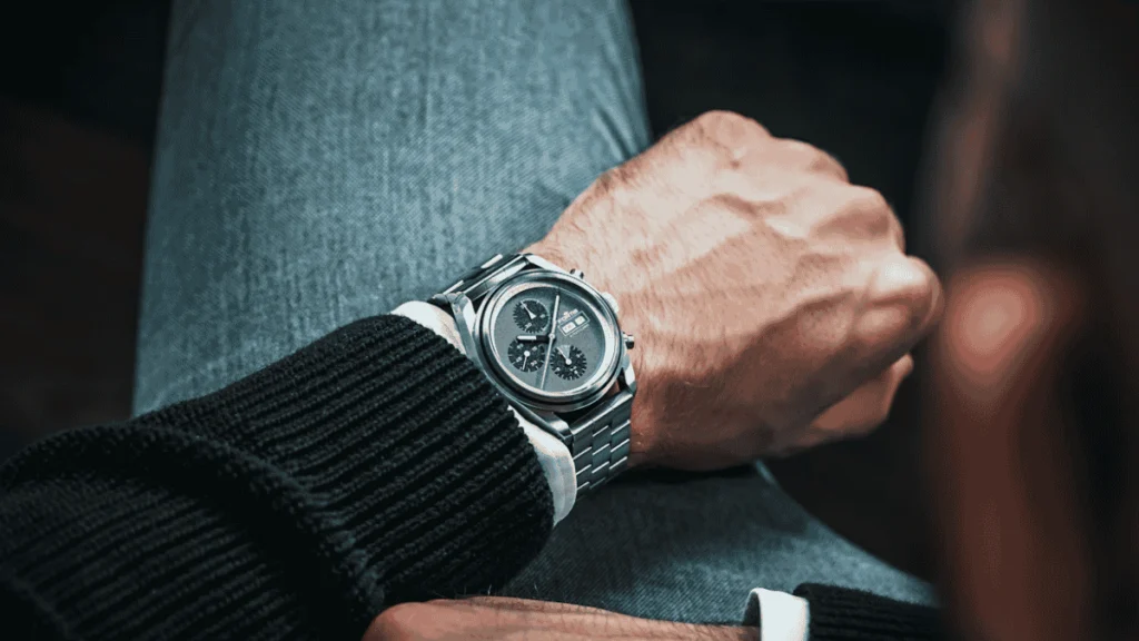 Close-up do pulso de um homem usando um relógio cronógrafo Fortis Stratoliner com pulseira de aço e mostrador cinza.