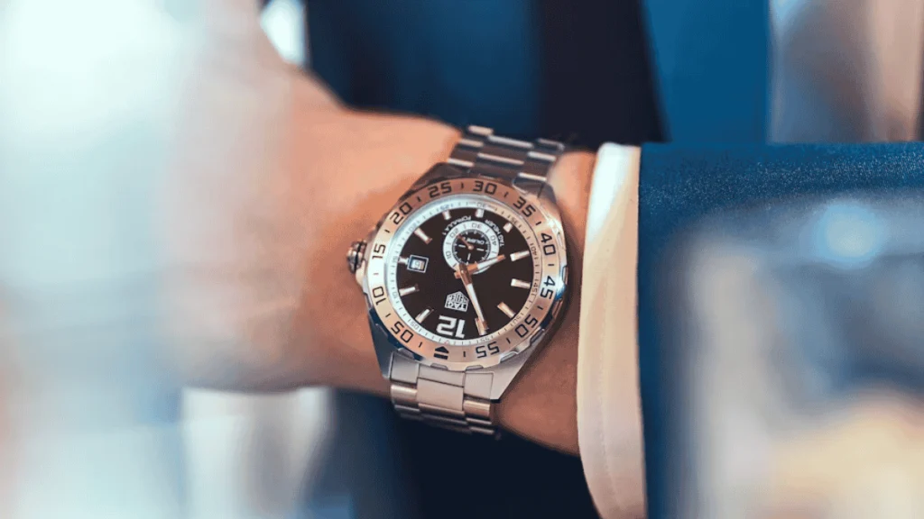 Relógio de pulso em aço inoxidável sob o punho de um blazer azul marinho, demonstrando elegância e caimento ideal.
